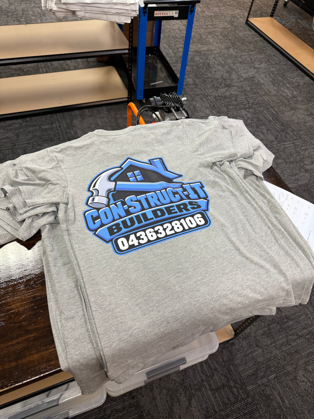 A grey shirt with Con-Struct-It Builders business artwork printed on the back.