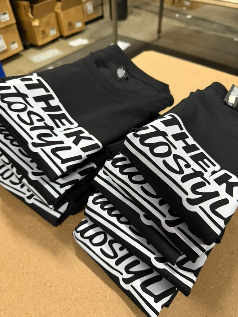 Stacks of black tees with a bold white typographic print, photographed in the print room.