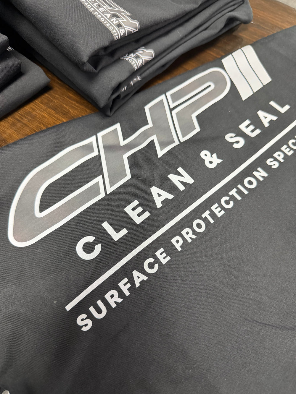 CHP Clean and Seal logo printed on black material, with folded matching shirts behind.